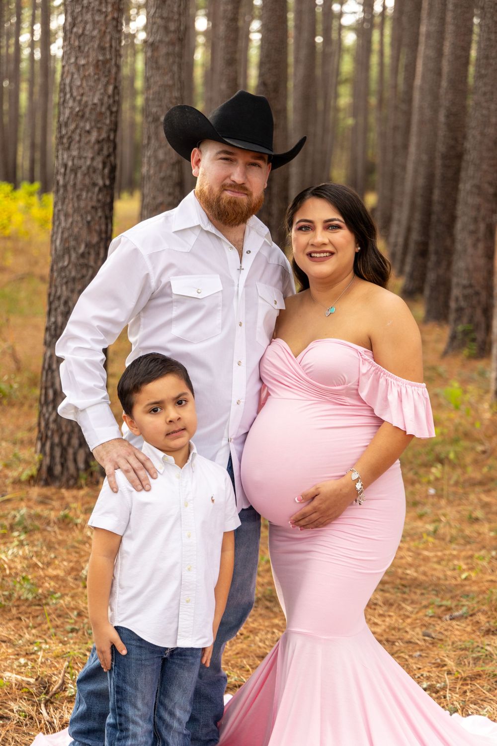 A family poses together in a pine forest with matching pink and white outfits.