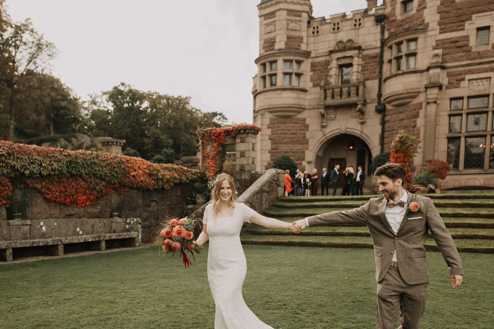 Couple celebrates their wedding day in front of a majestic Victorian-style mansion with stone architecture.