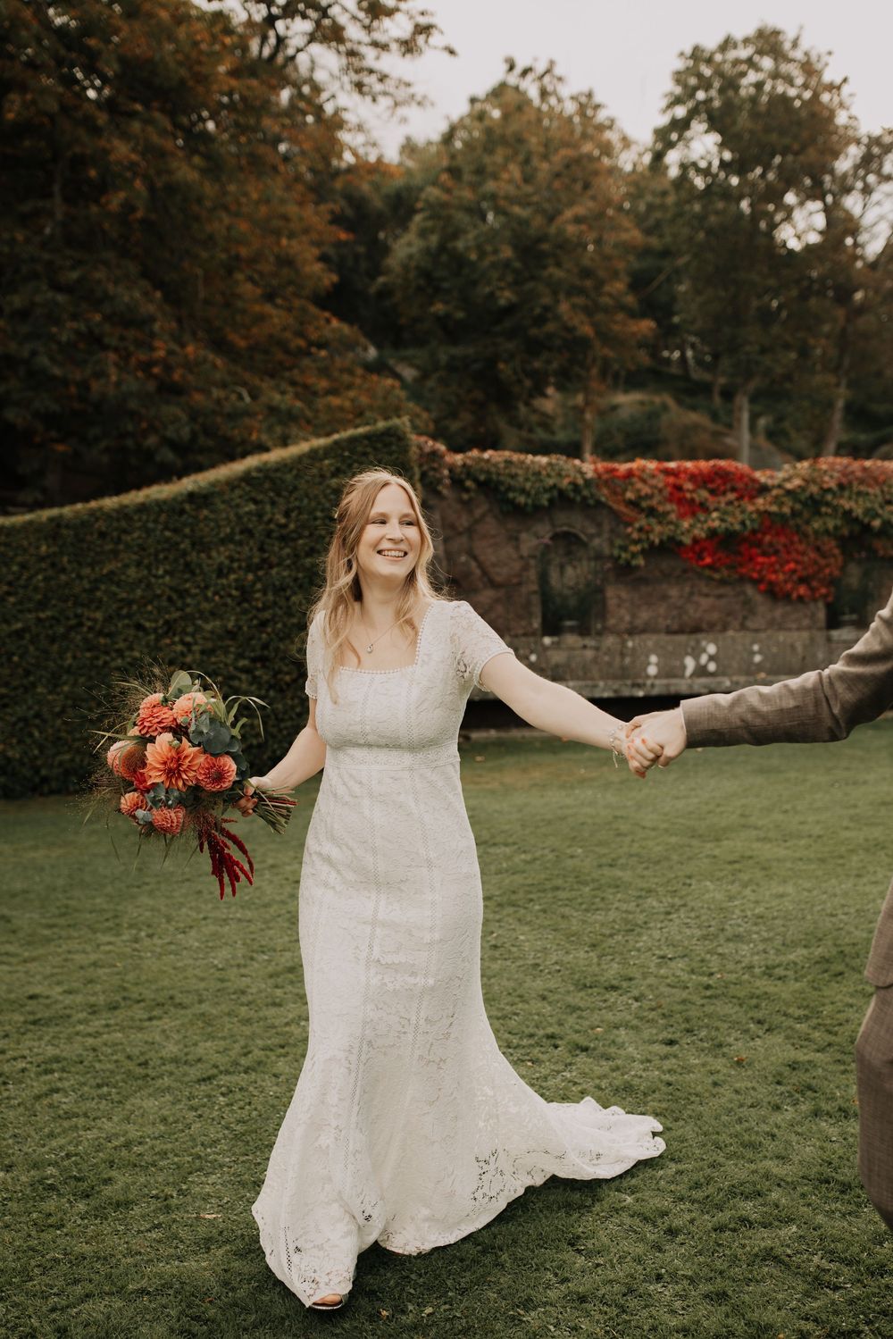 A joyful moment captured on a grassy lawn with flowing white dress and coral bouquet.