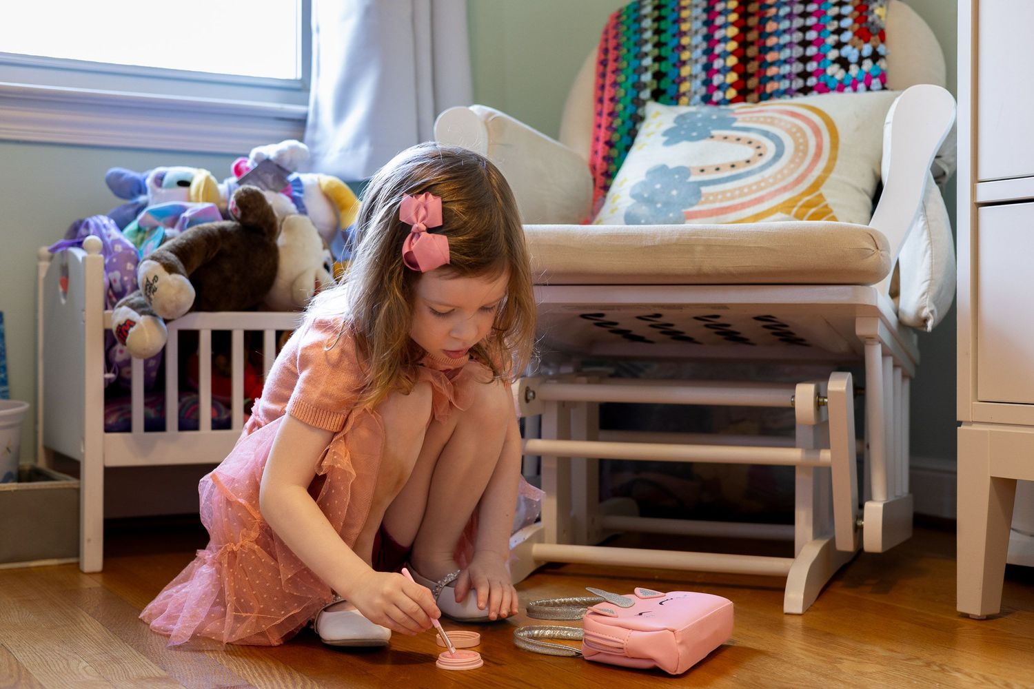 A young girl sits on the floor in a colorful room, playing with toys and books.