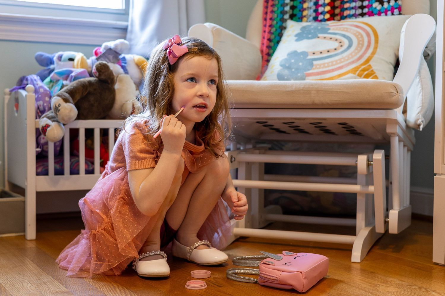 A young girl in a pink dress sits on the floor, playing with toys in a colorful bedroom.