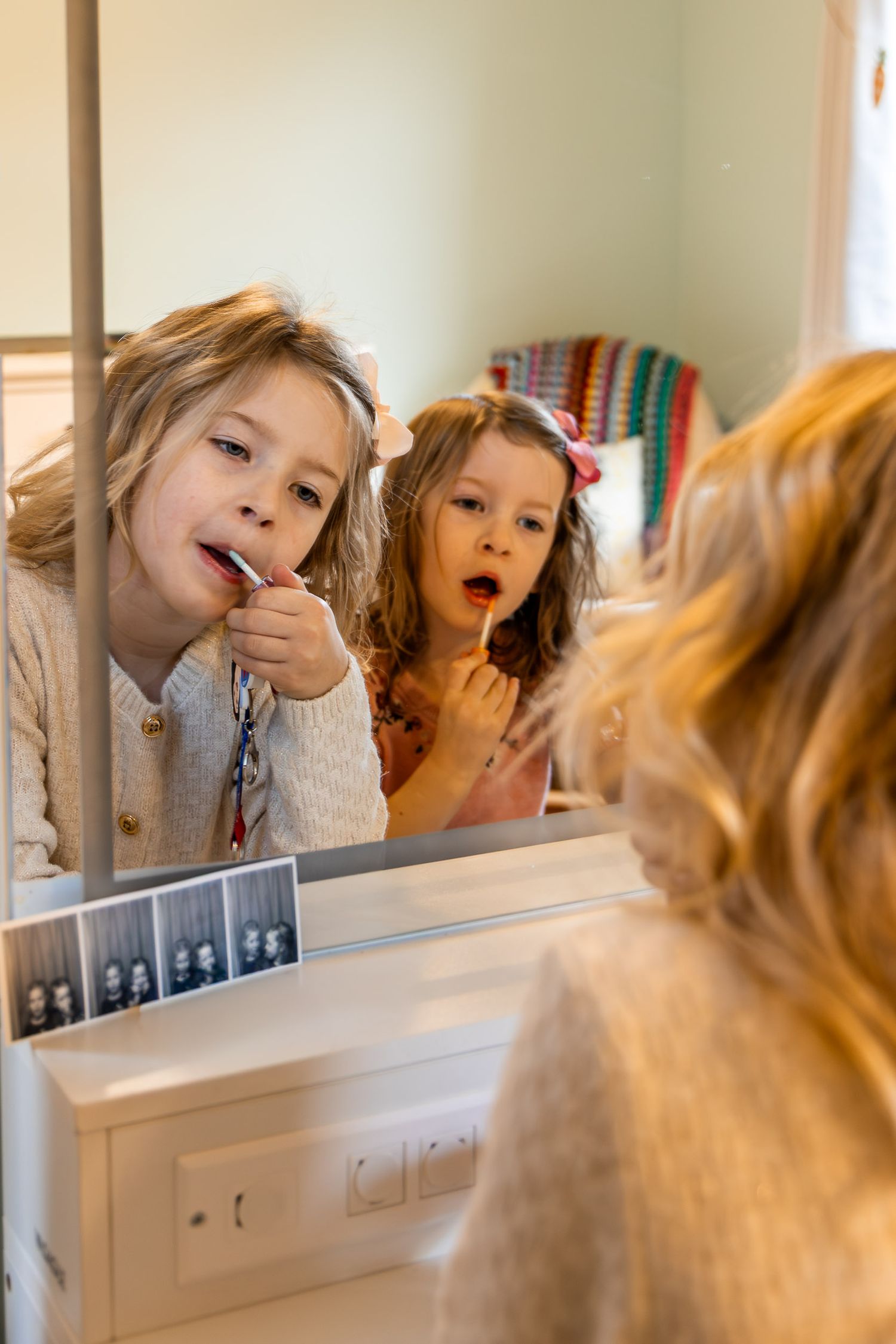Children making silly faces while looking at themselves in a bathroom mirror.