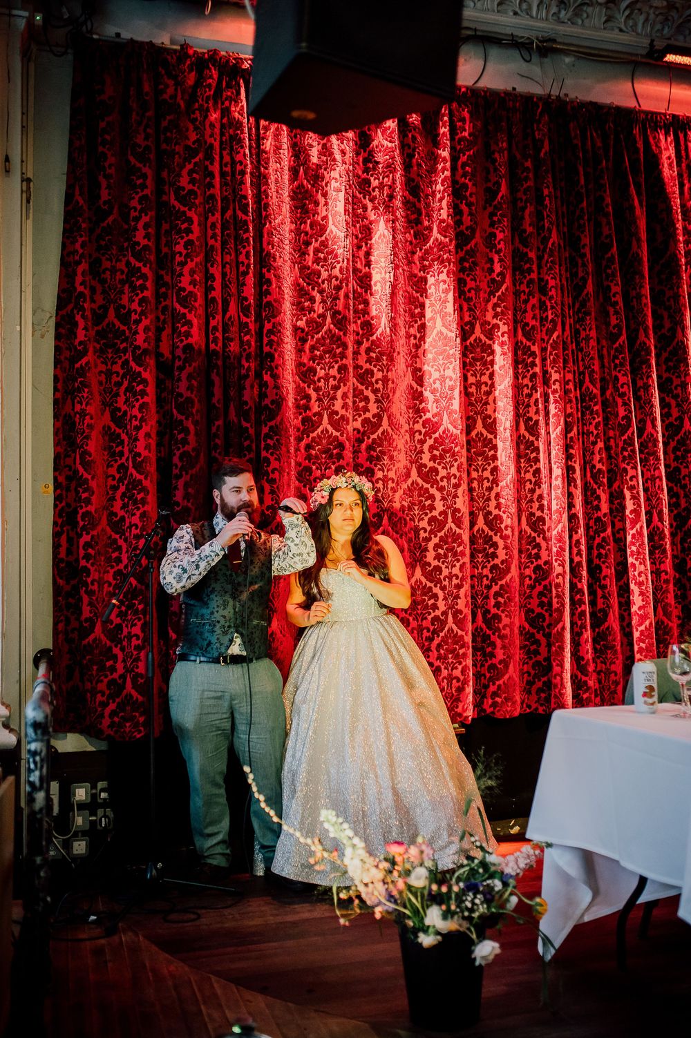 Wedding couple dances together in front of dramatic red velvet curtains during their reception celebration.