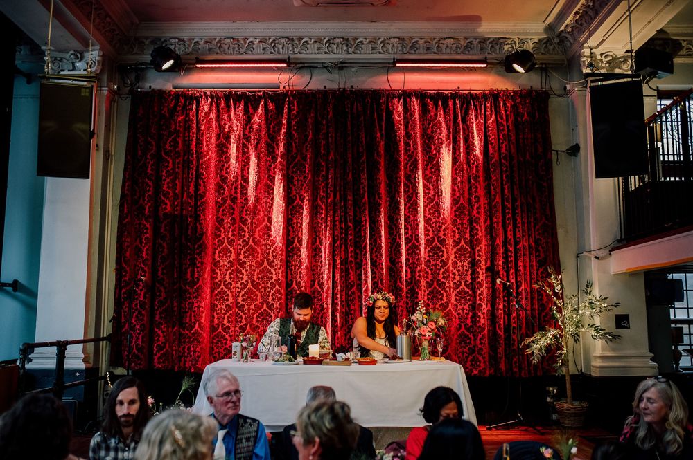 A dimly lit theater stage with red velvet curtains and ornate architectural details illuminated by warm lighting.