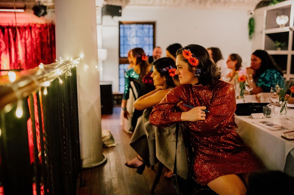 Guests dancing and celebrating at a dimly lit indoor wedding reception with red lighting accents.