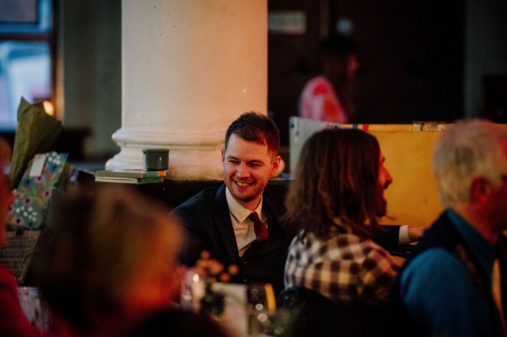 Wedding reception guests mingle and dance in a warmly lit venue with orange ambient lighting.