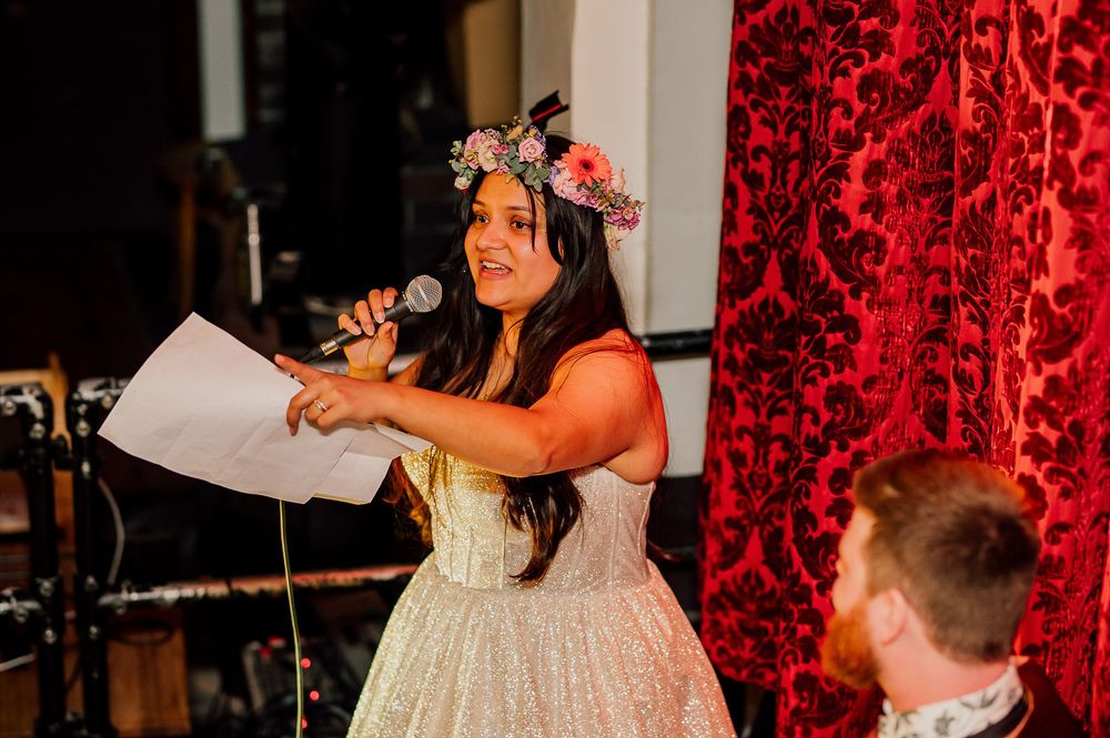 A couple shares a romantic dance moment at a wedding reception with red damask curtains in the background.