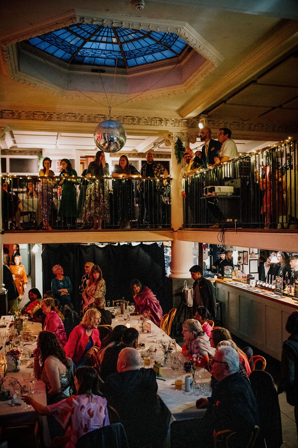 Guests gather at an elegant indoor venue with ornate ceiling details and ambient lighting during an evening event.