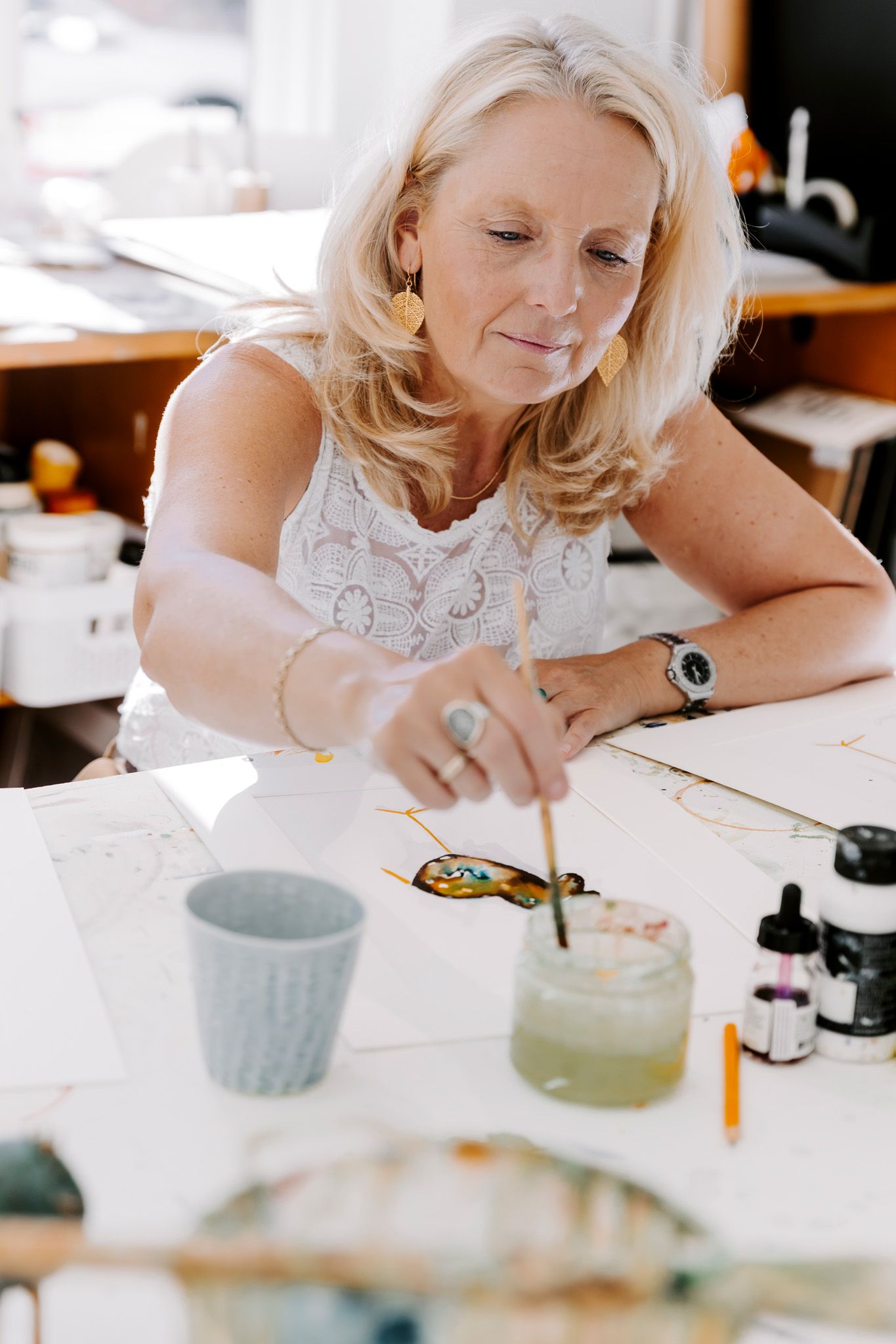 Kunstner maler en farverig fugleillustration på hvidt papir med akvarel og blæk ved et lyst studiebord. Fotograf Middelfart.
