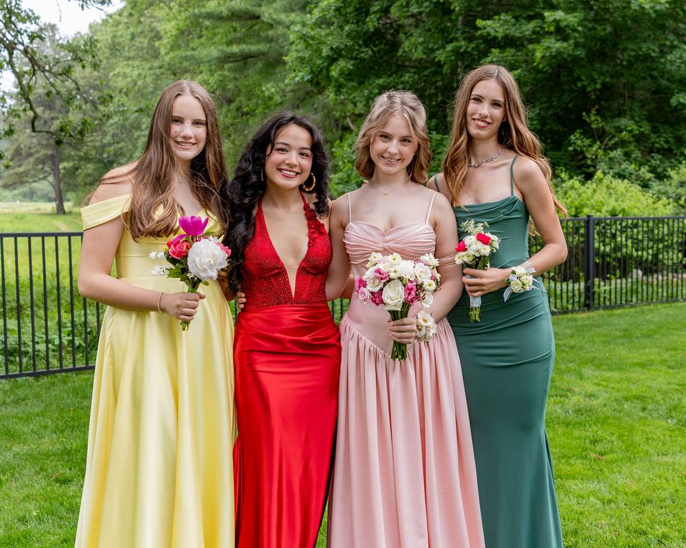 Four young women in elegant prom gowns in yellow, red, pink, and green hold bouquets outdoors at pre-prom photos in Weston, MA.