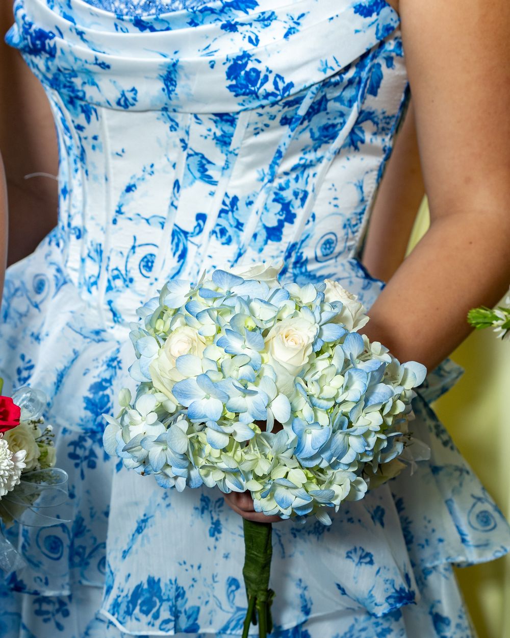 A young woman in blue floral dress holding white hydrangea and rose bouquet at at pre prom party in Weston, MA in Metrowest area of Boston