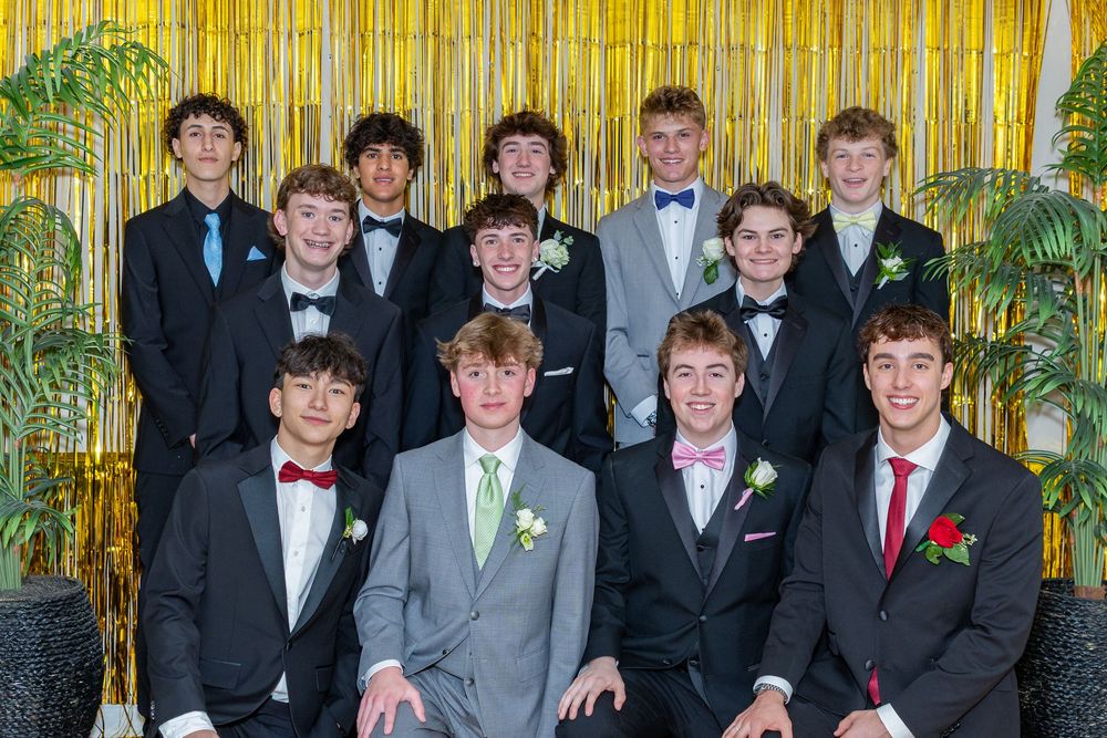 Teenage boys in formal tuxedos and suits posing together at prom in front of gold tinsel backdrop at pre prom party in Sudbury, MA.