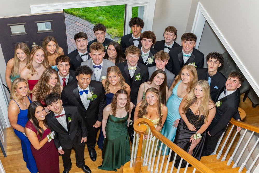 Large group of teens in formal prom attire posing on staircase, boys in tuxedos and girls in colorful gowns for pre-prom photos in Sudbury.