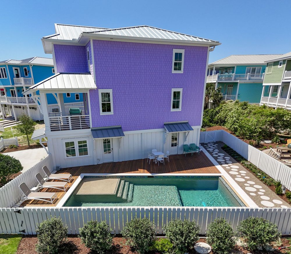 A vibrant purple beach house with a private swimming pool and white picket fence in a coastal neighborhood.