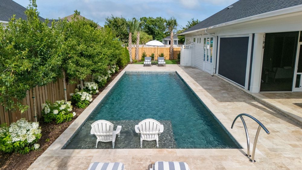 Sleek modern lap pool with two white Adirondack chairs on stone patio beside contemporary house and landscaping.