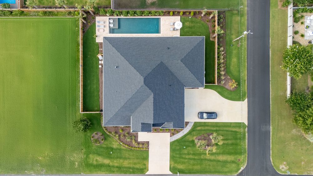 Aerial view of a modern home with gray roof and swimming pool surrounded by manicured green lawn.