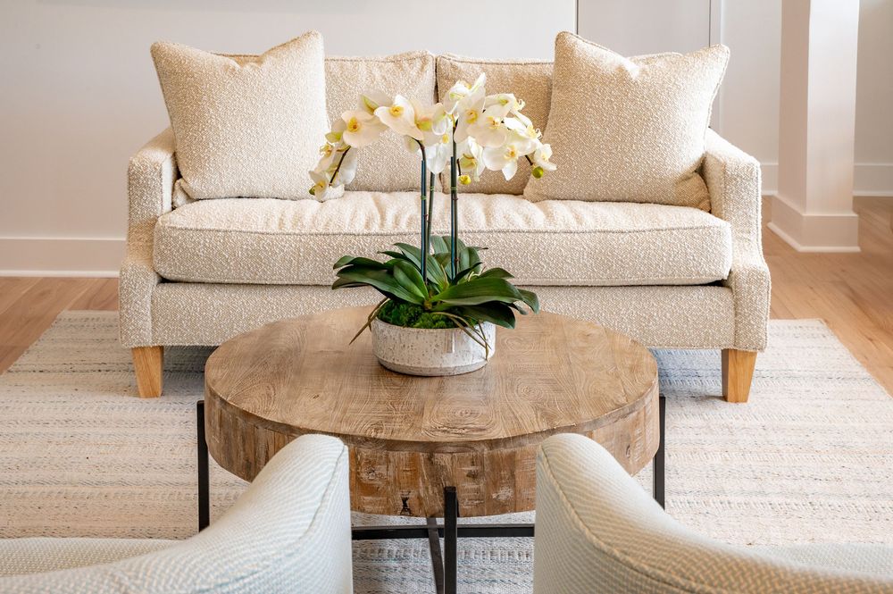 Modern living room interior with beige sofa, round coffee table and natural light streaming through windows.
