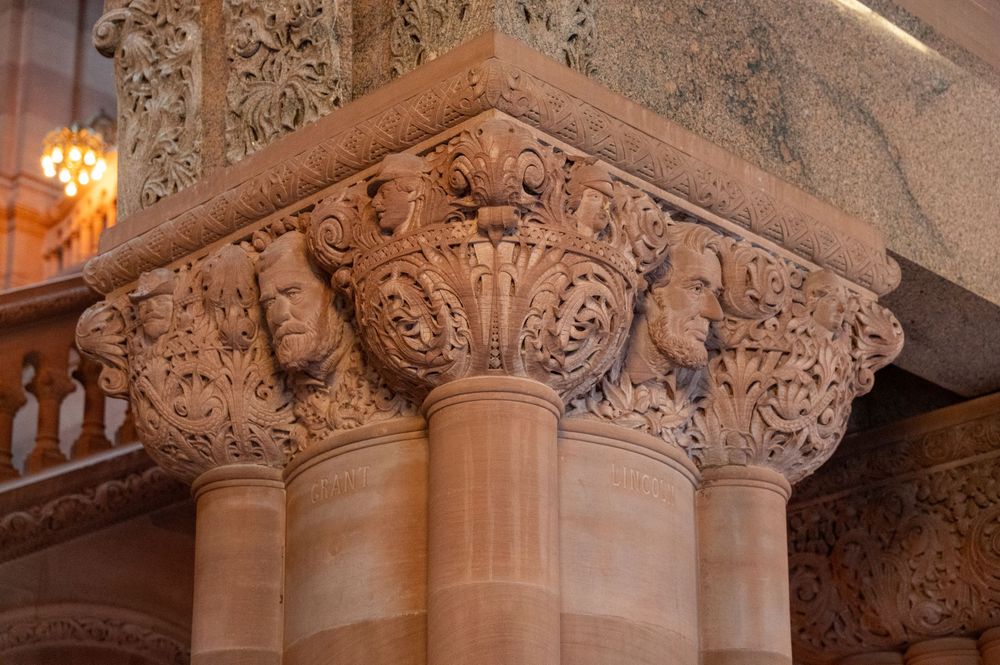 Ornate carved stone column capitals with decorative faces and floral motifs adorn historic architecture.