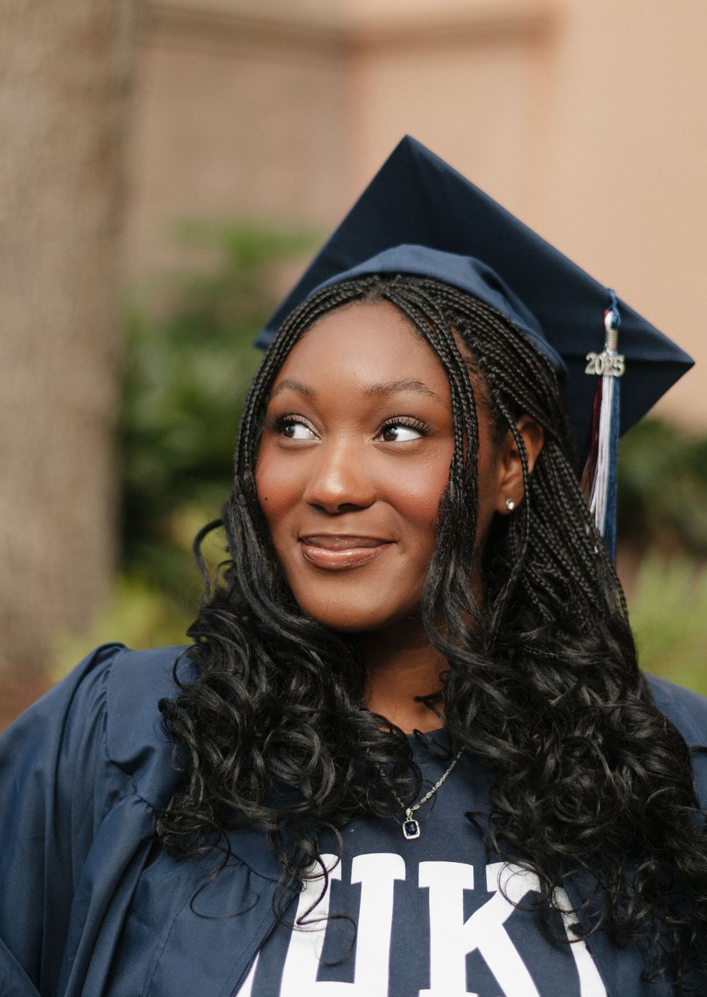 Graduate in black cap and gown smiling while looking to the side during outdoor graduation photo session.