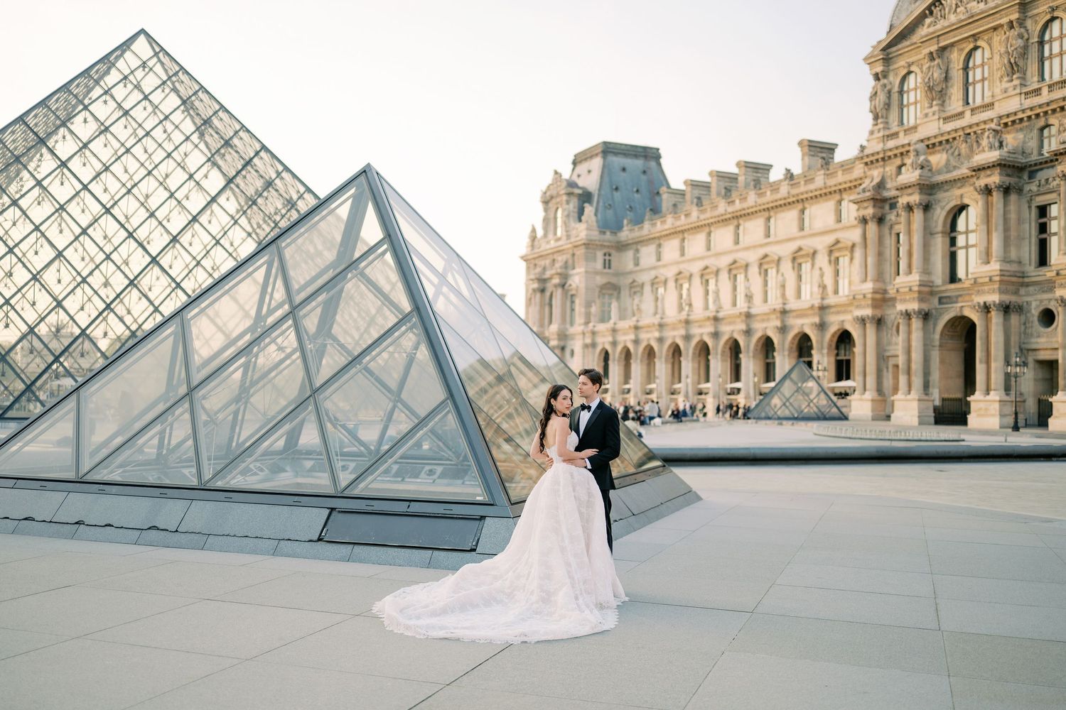 A wedding couple poses for romantic photos in front of the iconic glass pyramid at the Louvre Museum in Paris.