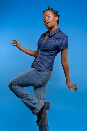 Photo of a girl in a full jean blue outfit, in front of a blue backdrop, mid dance, looking at the camera
