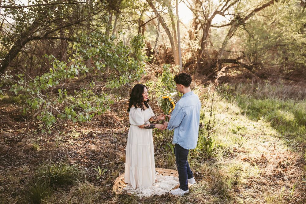 A couple shares an intimate moment in a sunlit wooded area during a romantic outdoor photoshoot.