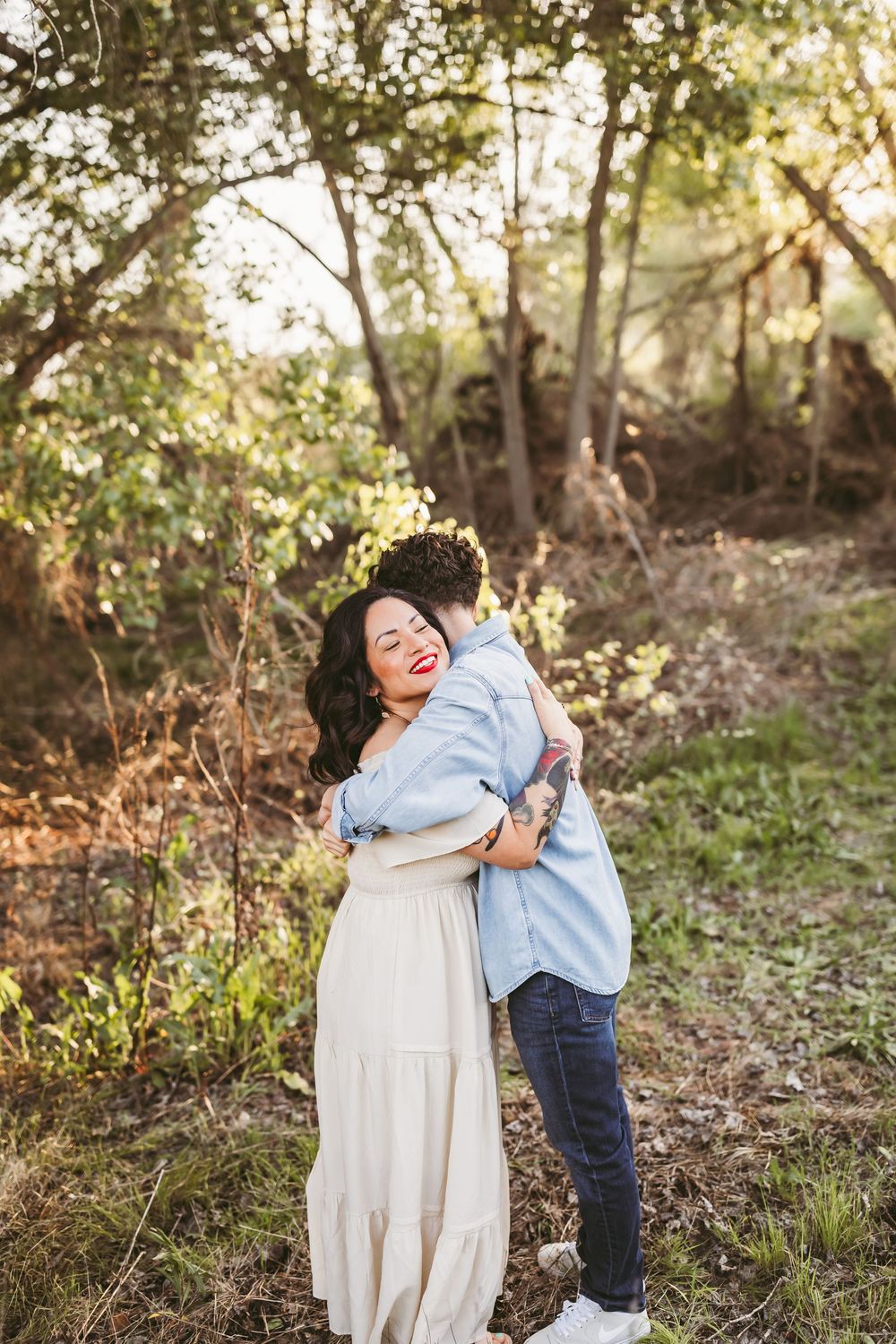A joyful couple shares a warm embrace while standing on a nature path during sunset.