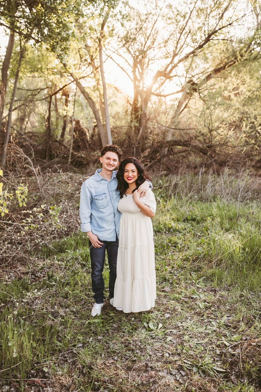 Couple enjoying a romantic sunset photoshoot in a wooded natural setting with golden light filtering through trees.