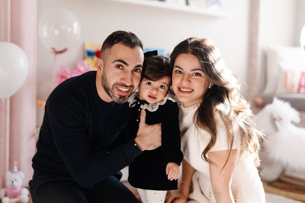 Happy family portrait with mother, father, and baby girl in a pink decorated nursery.