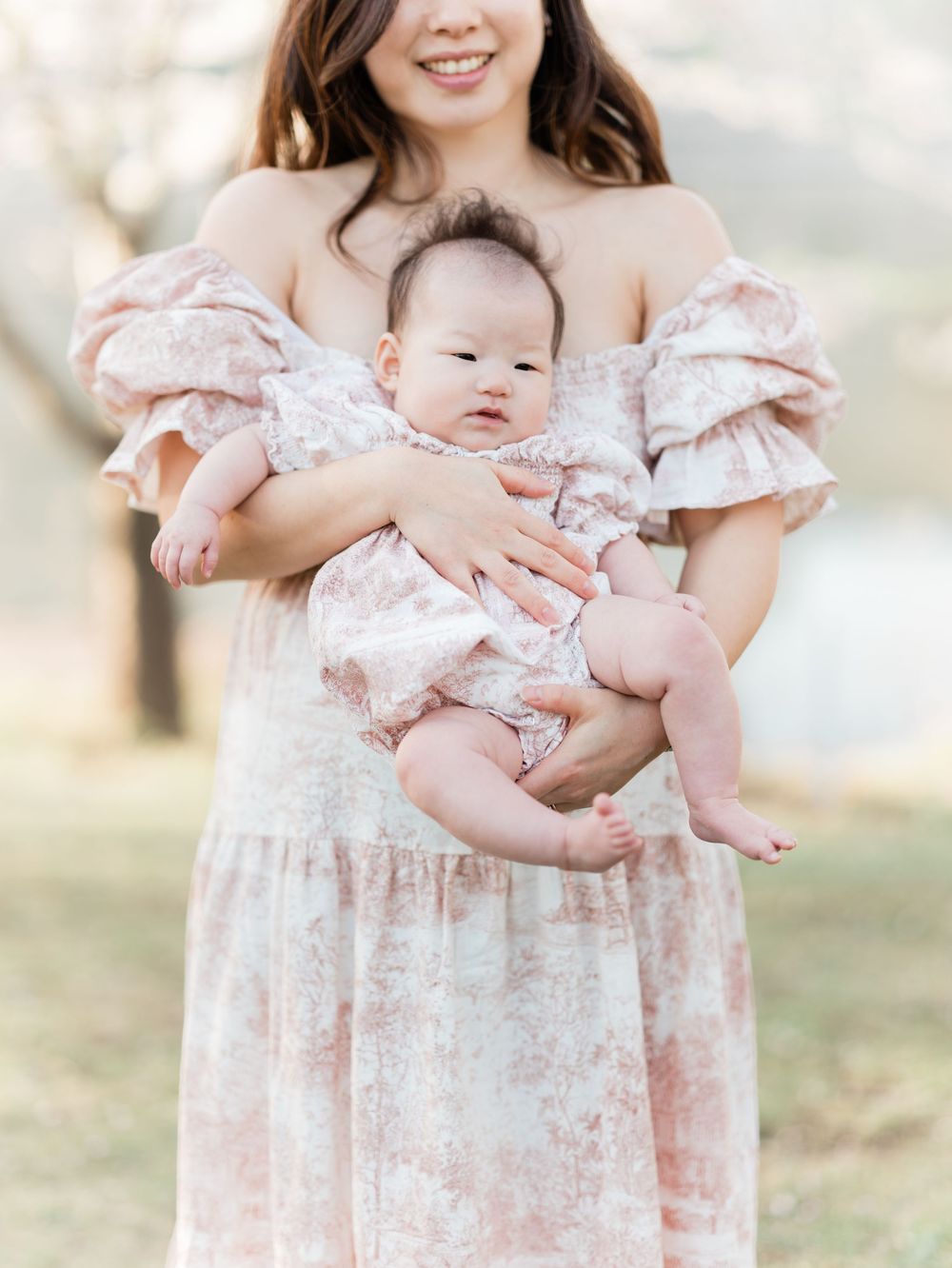 Mother in pink floral dress cradling smiling newborn baby.