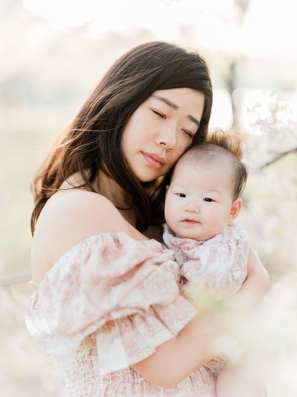 Mother tenderly embracing baby among white spring blossoms.