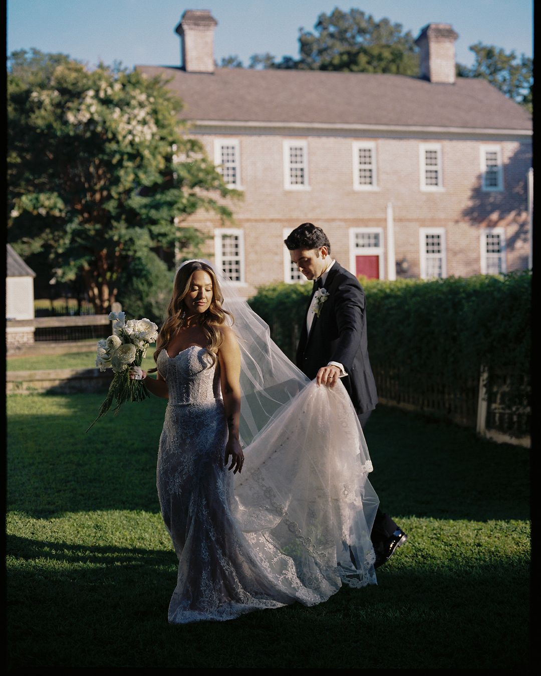 Wedding couple walking across a manicured lawn of a historic colonial estate.