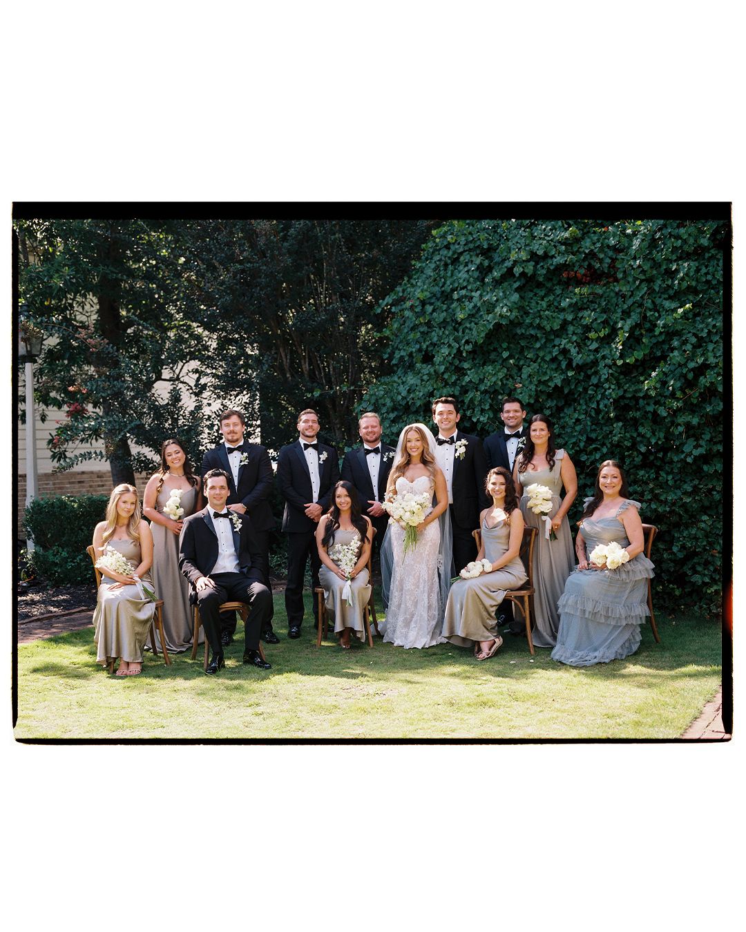 Wedding party lounges casually on grass in coordinated formal attire during outdoor summer photo session.