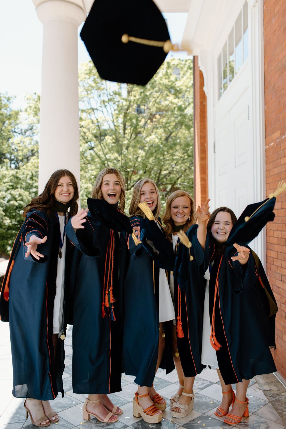 Graduates in black robes toss caps in celebration on campus portico.