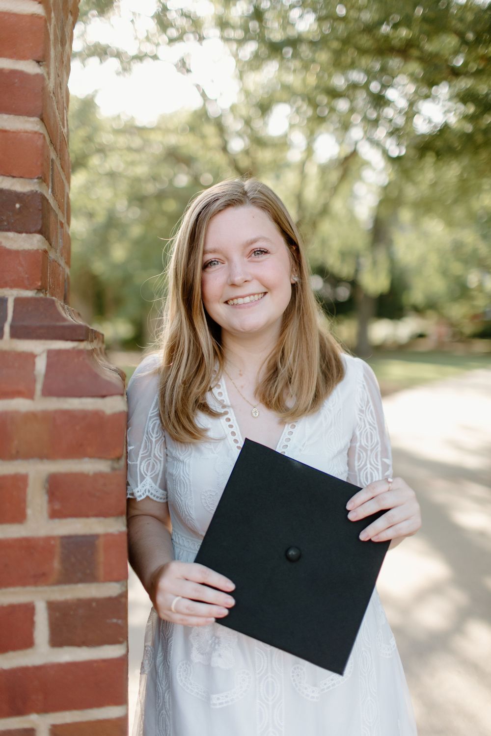 A graduate holds their diploma while standing next to a brick column outdoors.