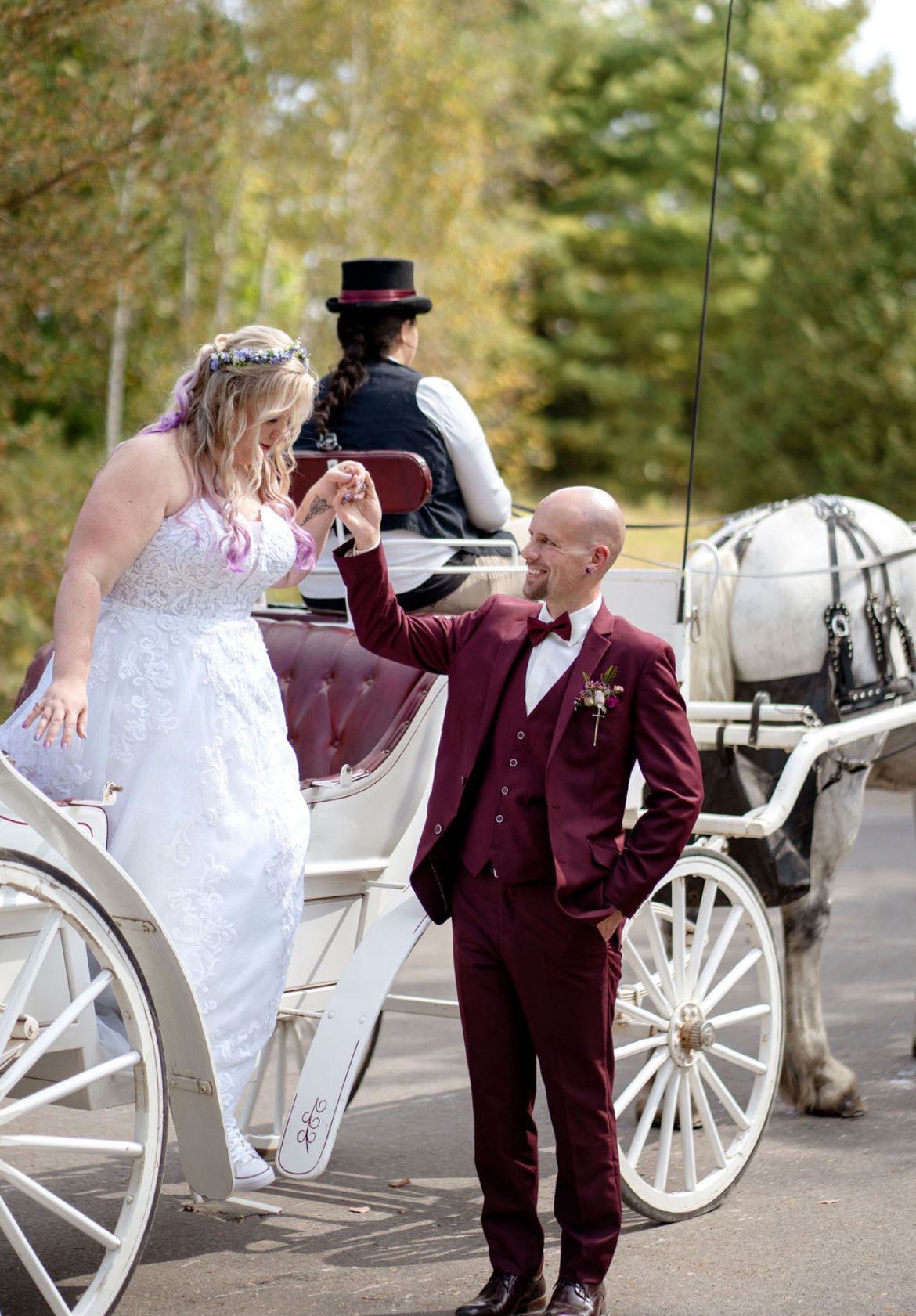 Photo of a groom assisting his bride out of a. horse drawn carriage at The Arboretum in Guelph ON