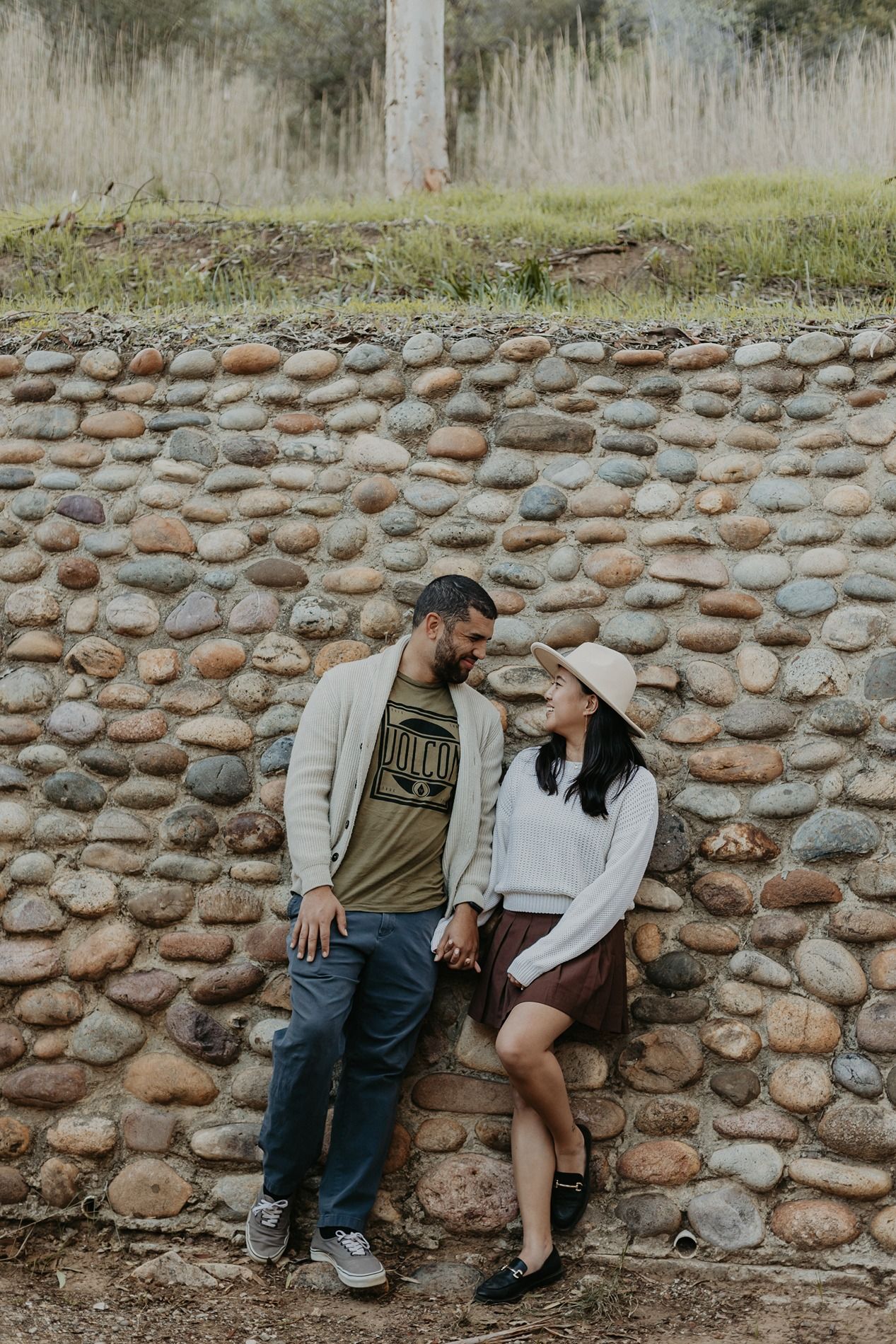 A couple sits together against a rustic stone wall outdoors in a casual romantic moment at Will Rogers State Park.