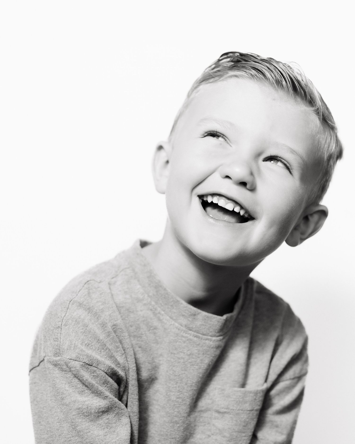 Black and white portrait of a young child laughing joyfully while wearing a gray sweatshirt against a white background.