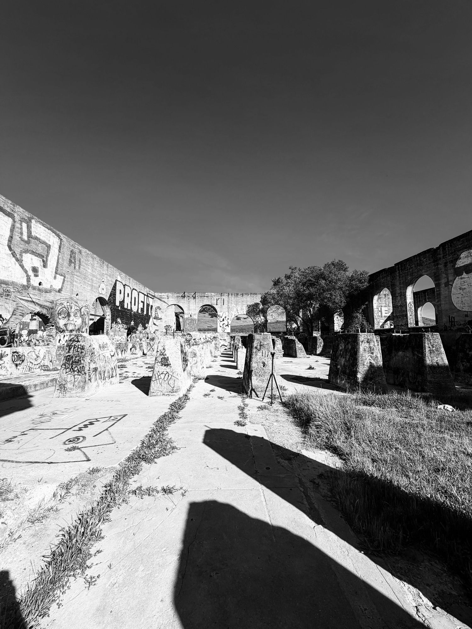 Black and white panoramic view of abandoned buildings and ruins along a hillside path in harsh sunlight.
