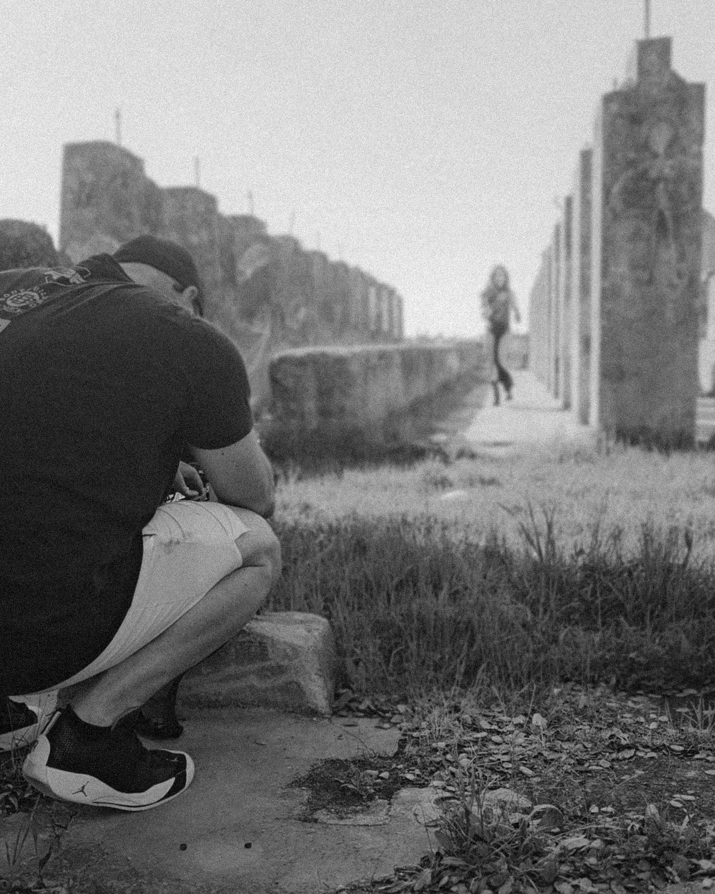 A black and white photo sequence shows a person crouching down in an urban setting with tall buildings in the background.