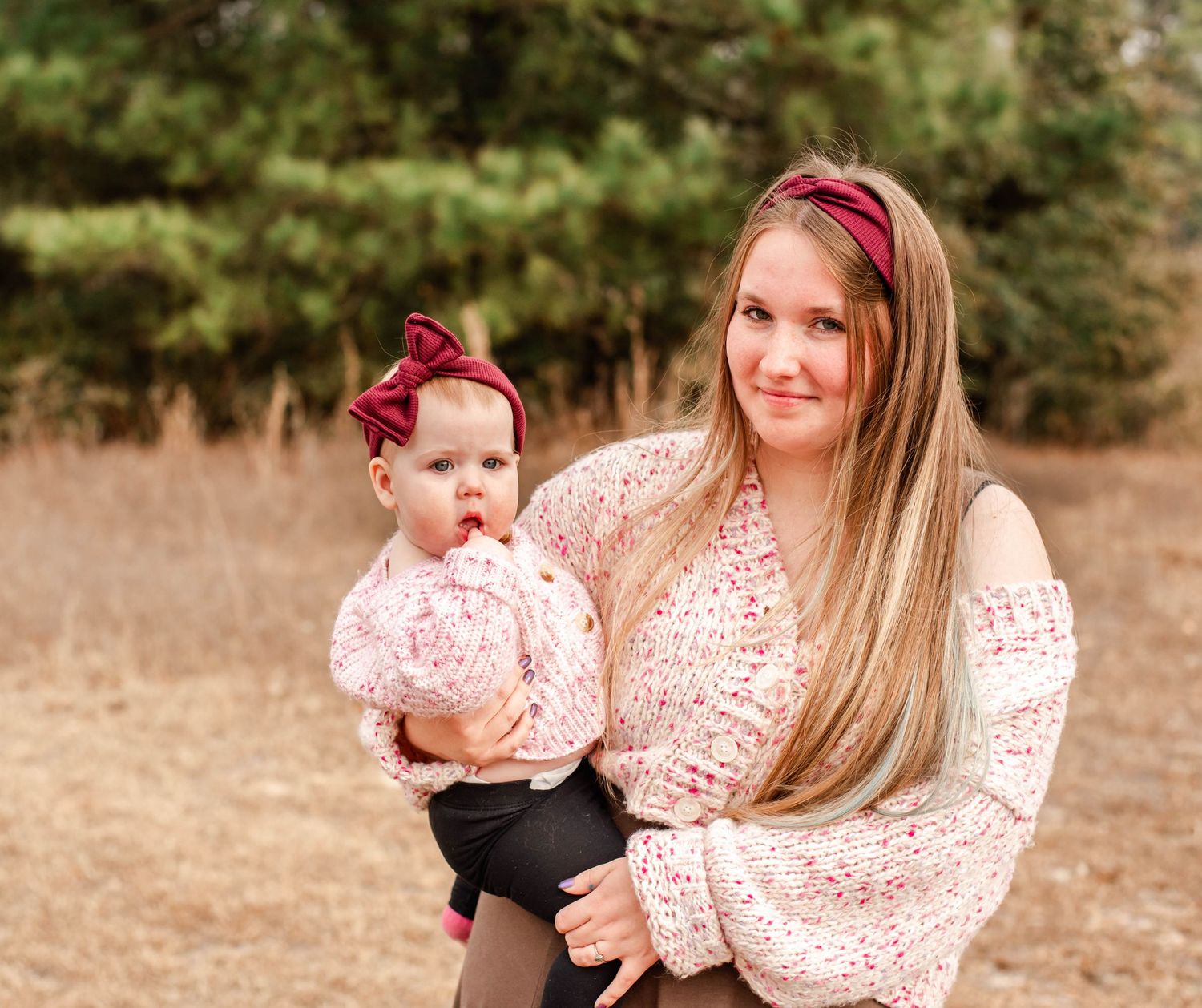 A parent and baby wearing matching pink floral outfits pose together in an outdoor autumn setting.