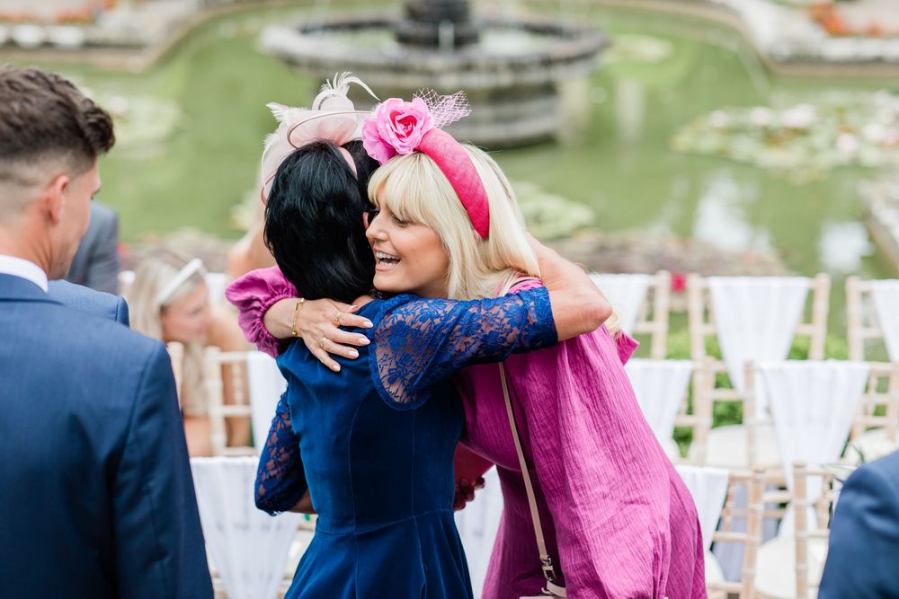 Wedding guests in formal attire hugging and celebrating at an outdoor venue.