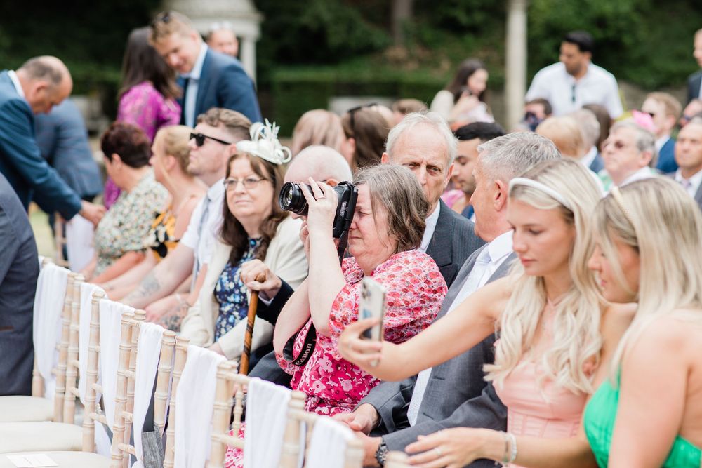 Wedding ceremony guests seated in white chairs decorated with floral arrangements outdoors at Italian Villa, Dorset