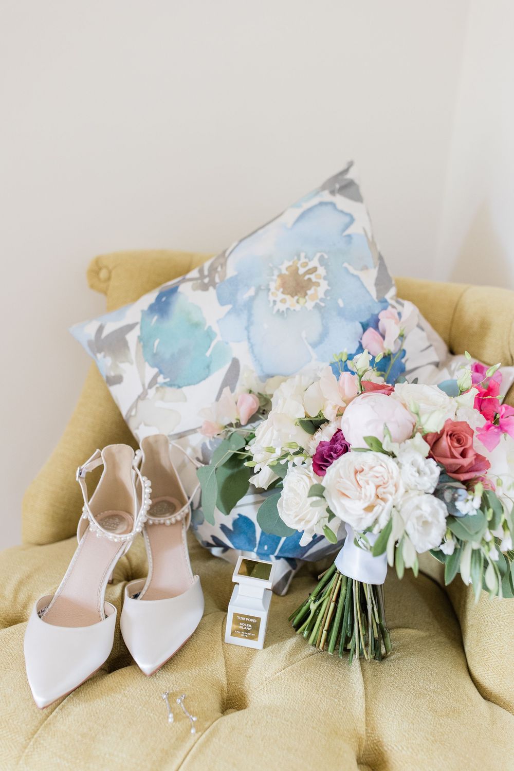 Elegant white bridal shoes and a pastel floral bouquet arranged on a armchair by Maddie Waters Photography