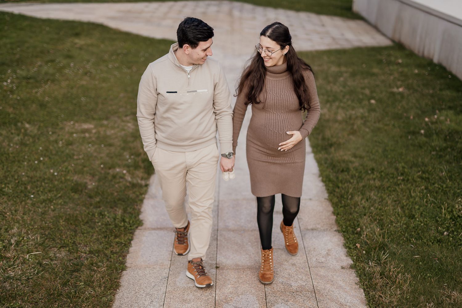 A couple walking together on a concrete path wearing coordinated neutral-toned outfits.