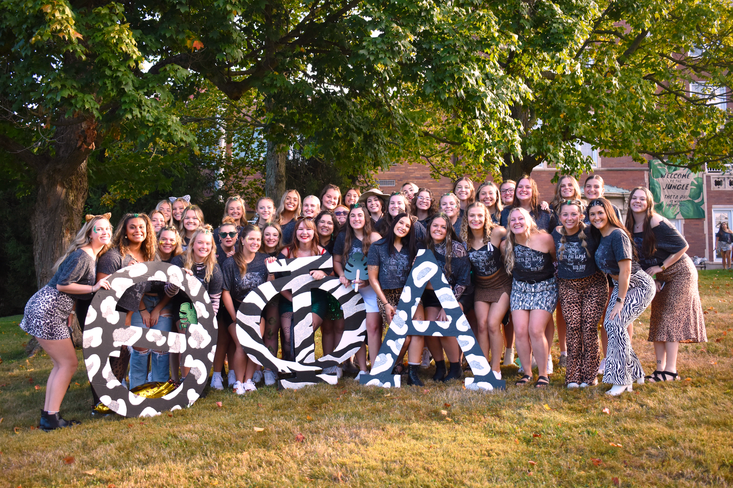 Large group photo of students posing with banners on a sunny lawn.