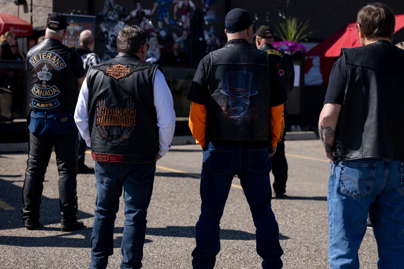 Group of motorcyclists wearing vests gathered in a parking lot.