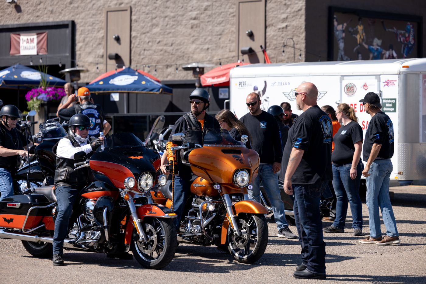 Motorcyclists gathered around orange and black motorcycles at an outdoor event.