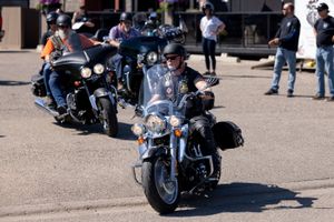 Motorcyclists riding through a parking area with spectators watching.