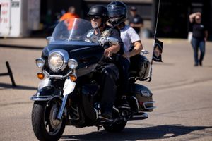 Two motorcyclists riding a large touring bike with a windshield in a parking area.